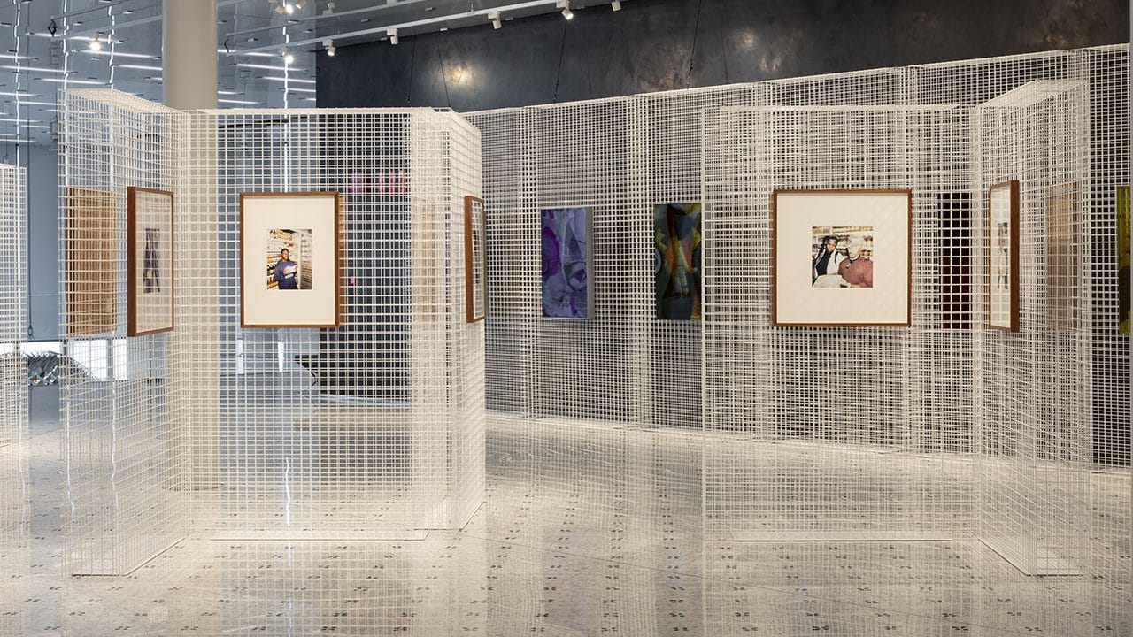 Sala della mostra con fotografie incorniciate appese a pareti di rete metallica bianca