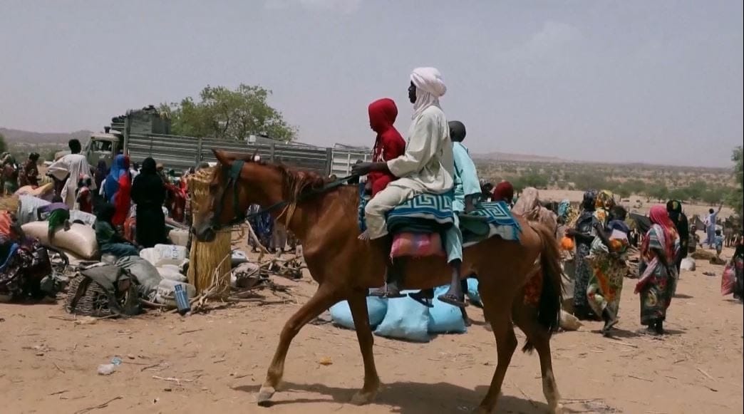 Un uomo e un bambino a cavallo attraversano un accampamento affollato, tra sacchi e teloni