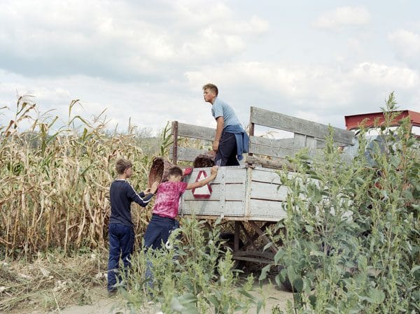 Un uomo e due bambini caricano un carro accanto a un campo di mais
