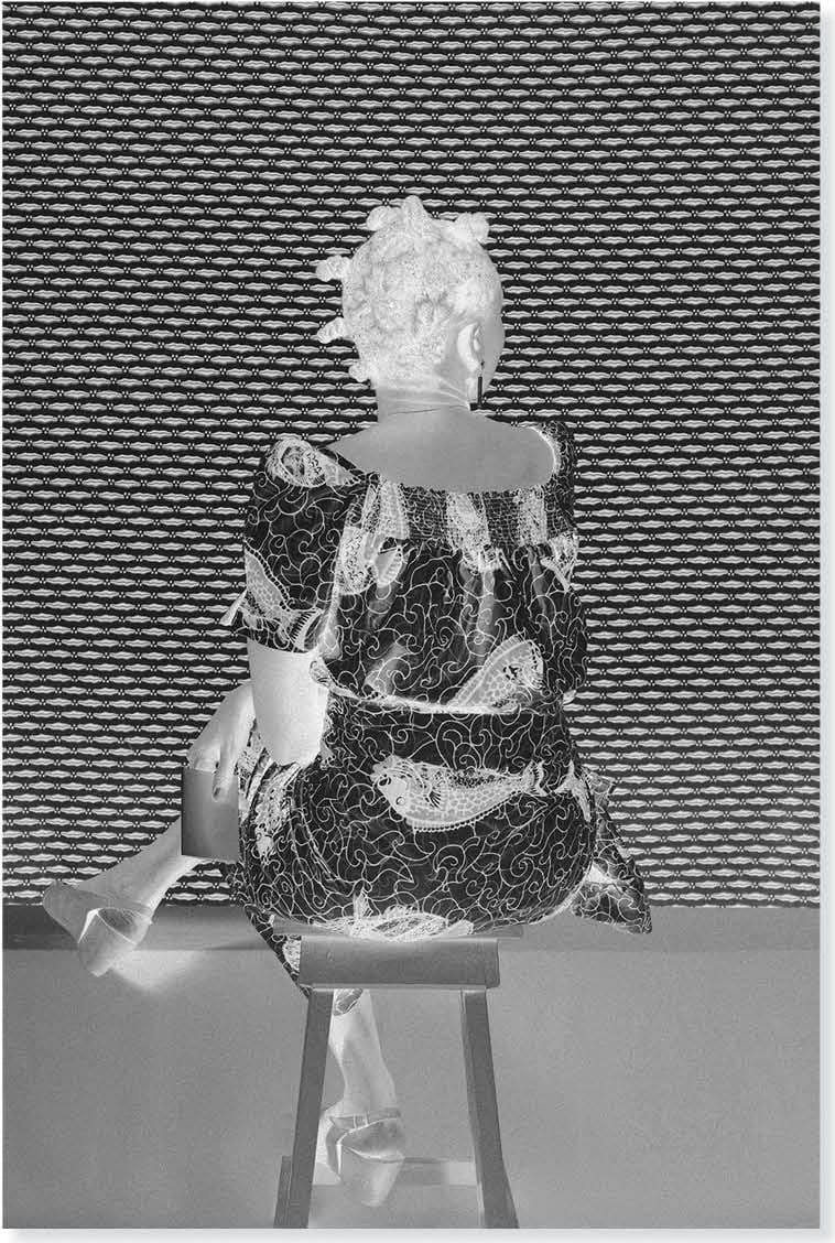 Fotografia di Silvia Rosi in bianco e nero: una donna seduta in un abito a motivi geometrici, davanti a un fondo a trama ripetuta