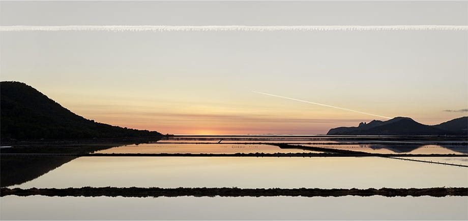 Saline al tramonto, con il cielo arancio riflesso nell’acqua e colline scure all’orizzonte