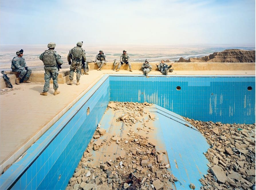 Uomini in uniforme seduti sul bordo di una piscina vuota e in rovina, nel deserto