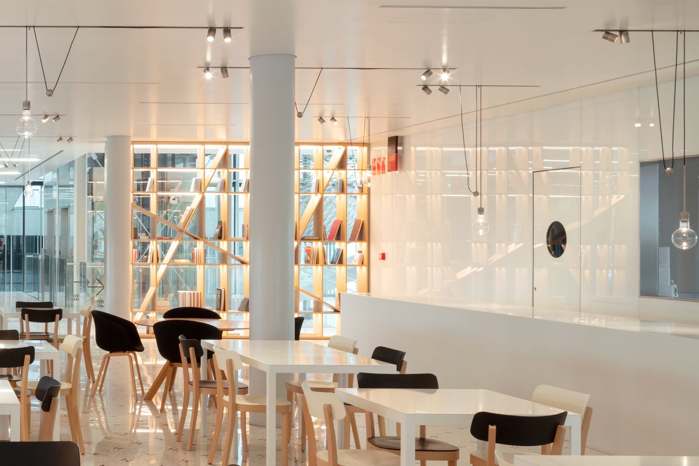 La Caffetteria: tavoli bianchi, sedie in legno e la libreria illuminata dei libri di fotografia