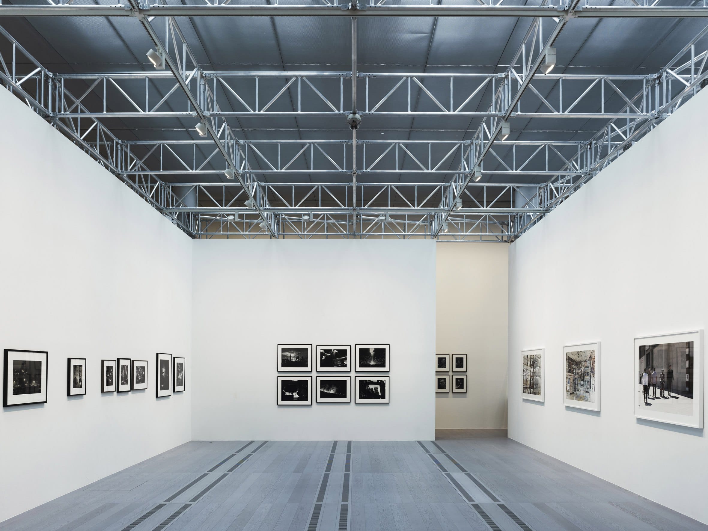 Una sala con la copertura in travi d’acciaio e fotografie in bianco e nero alle pareti