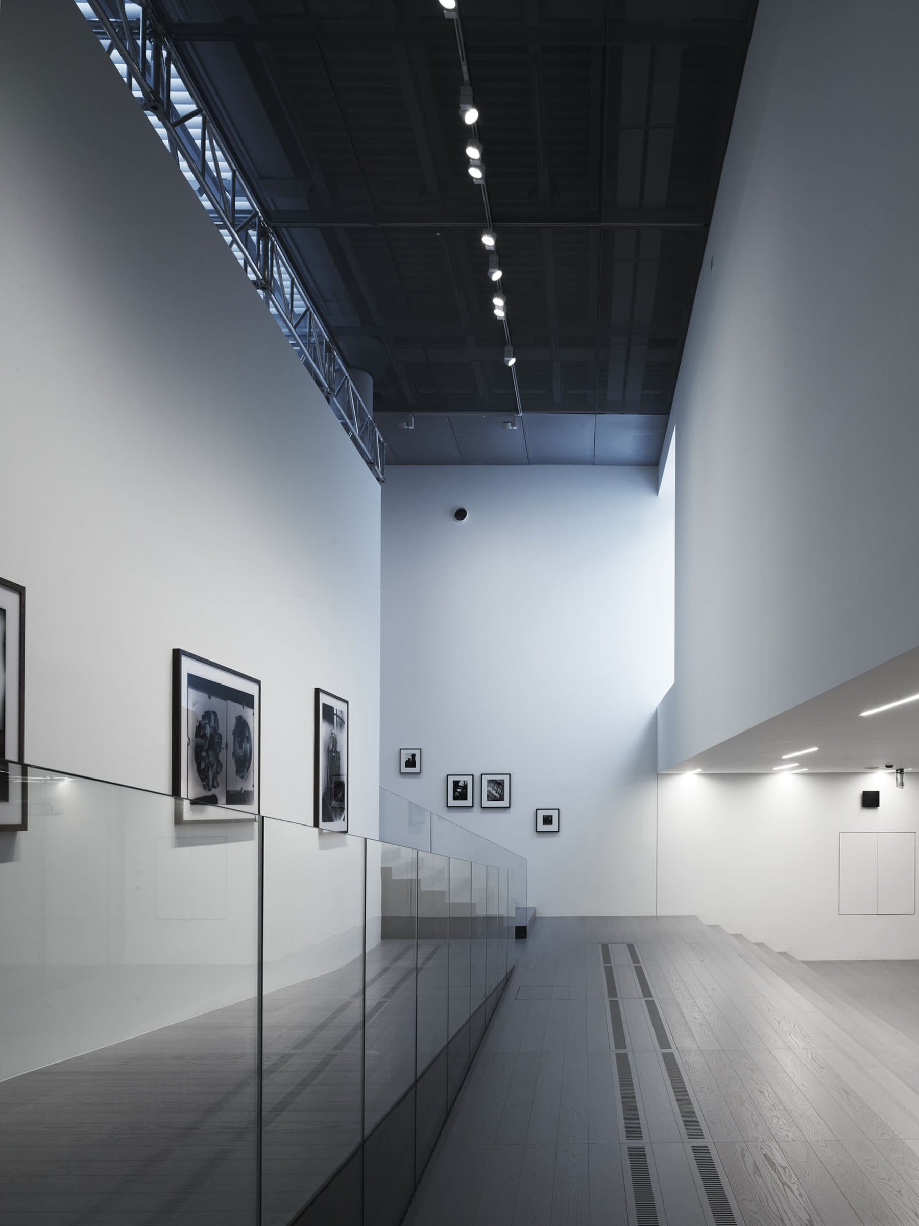 Una galleria lunga e alta, con le fotografie lungo la parete bianca e la luce dall’alto