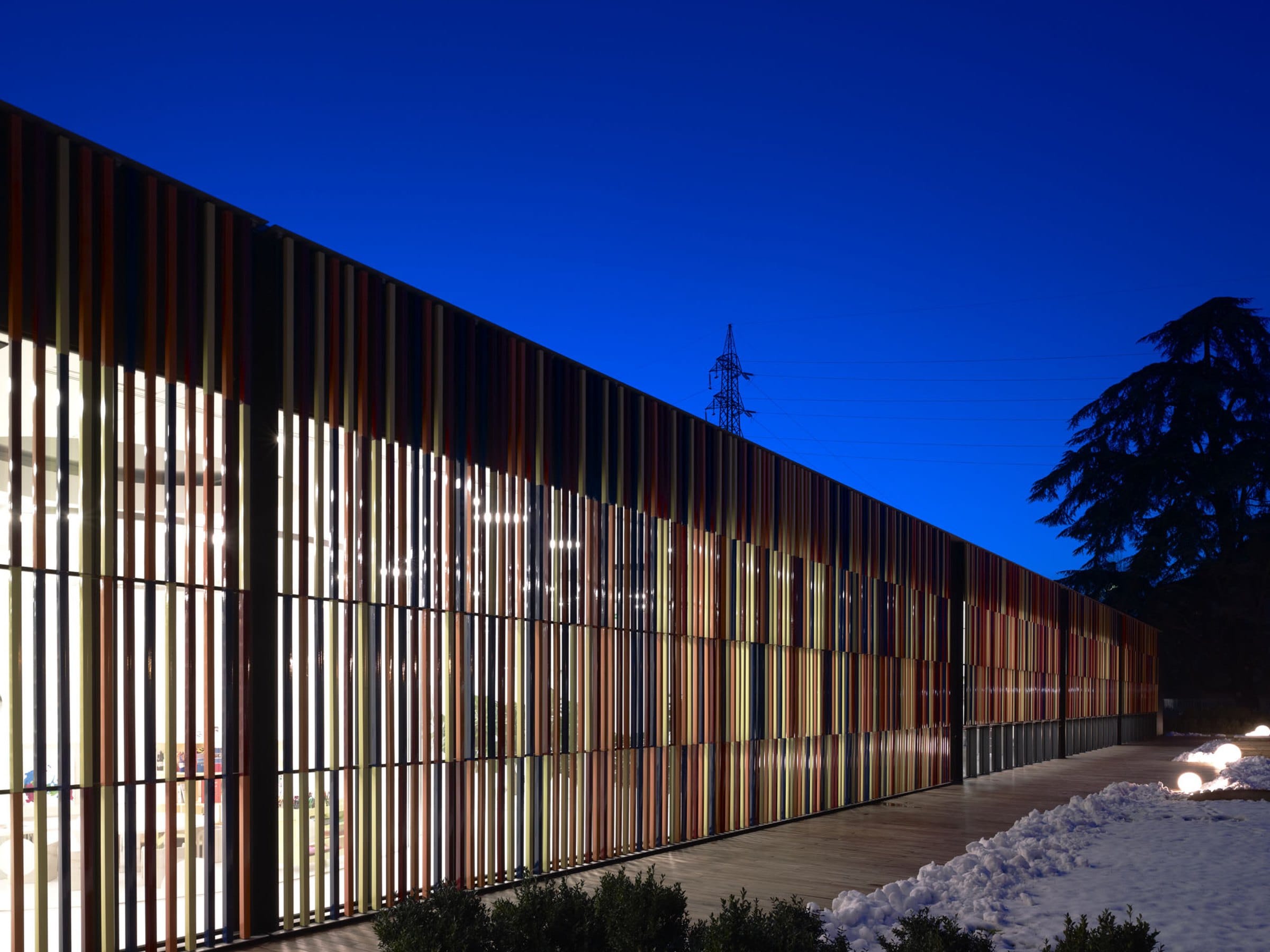 L’edificio del Nido Scuola di sera, con la facciata a lamelle colorate illuminate