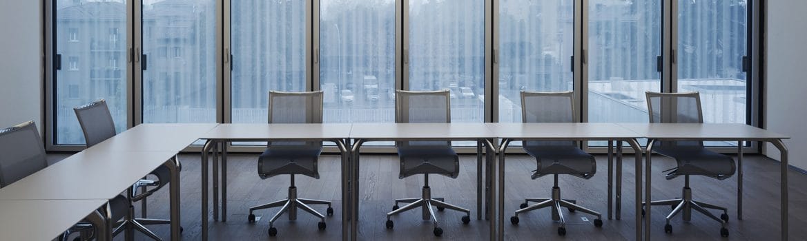 Un’aula vuota: tavoli bianchi e sedie davanti alle vetrate