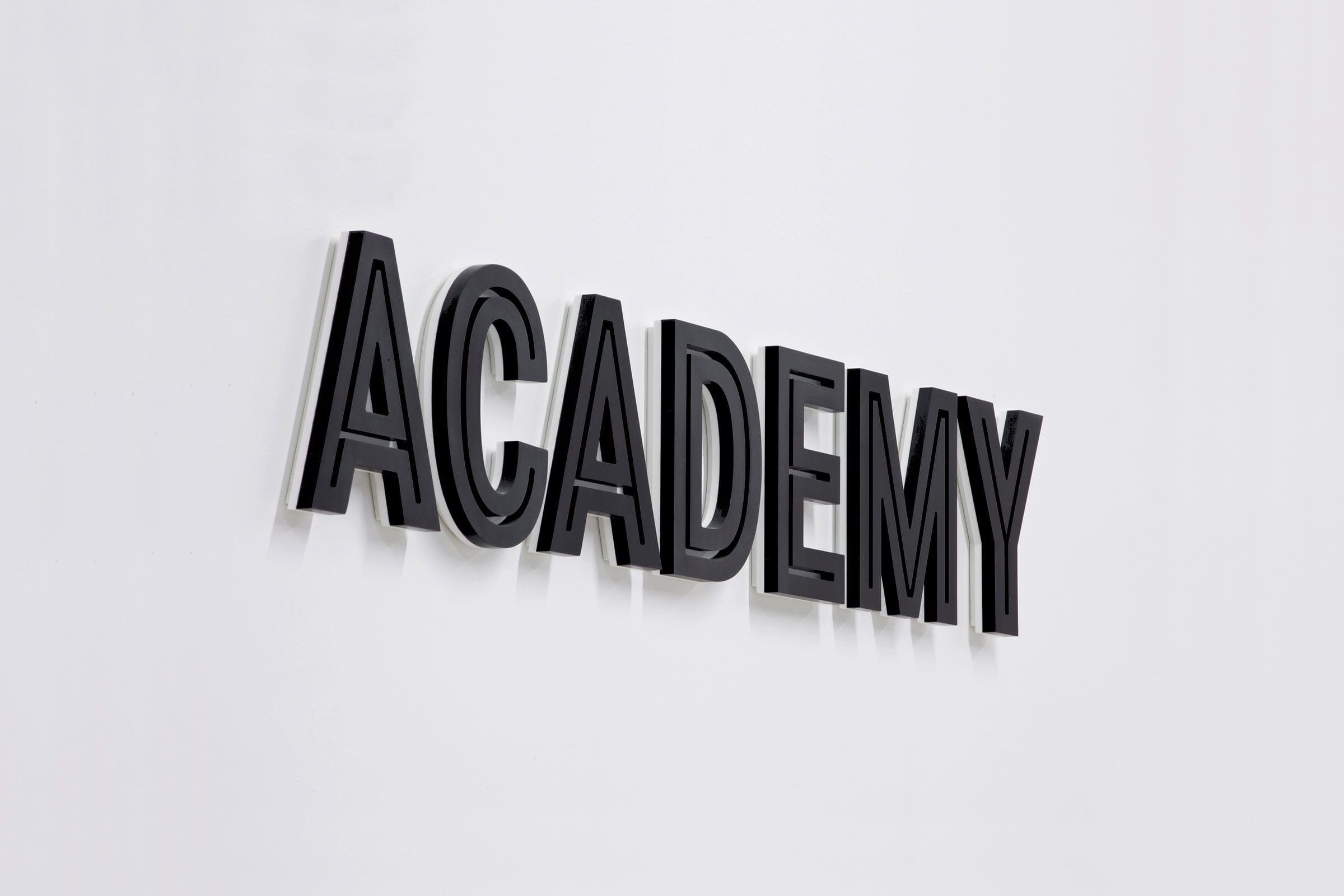 La scritta ACADEMY in lettere nere a rilievo su una parete bianca