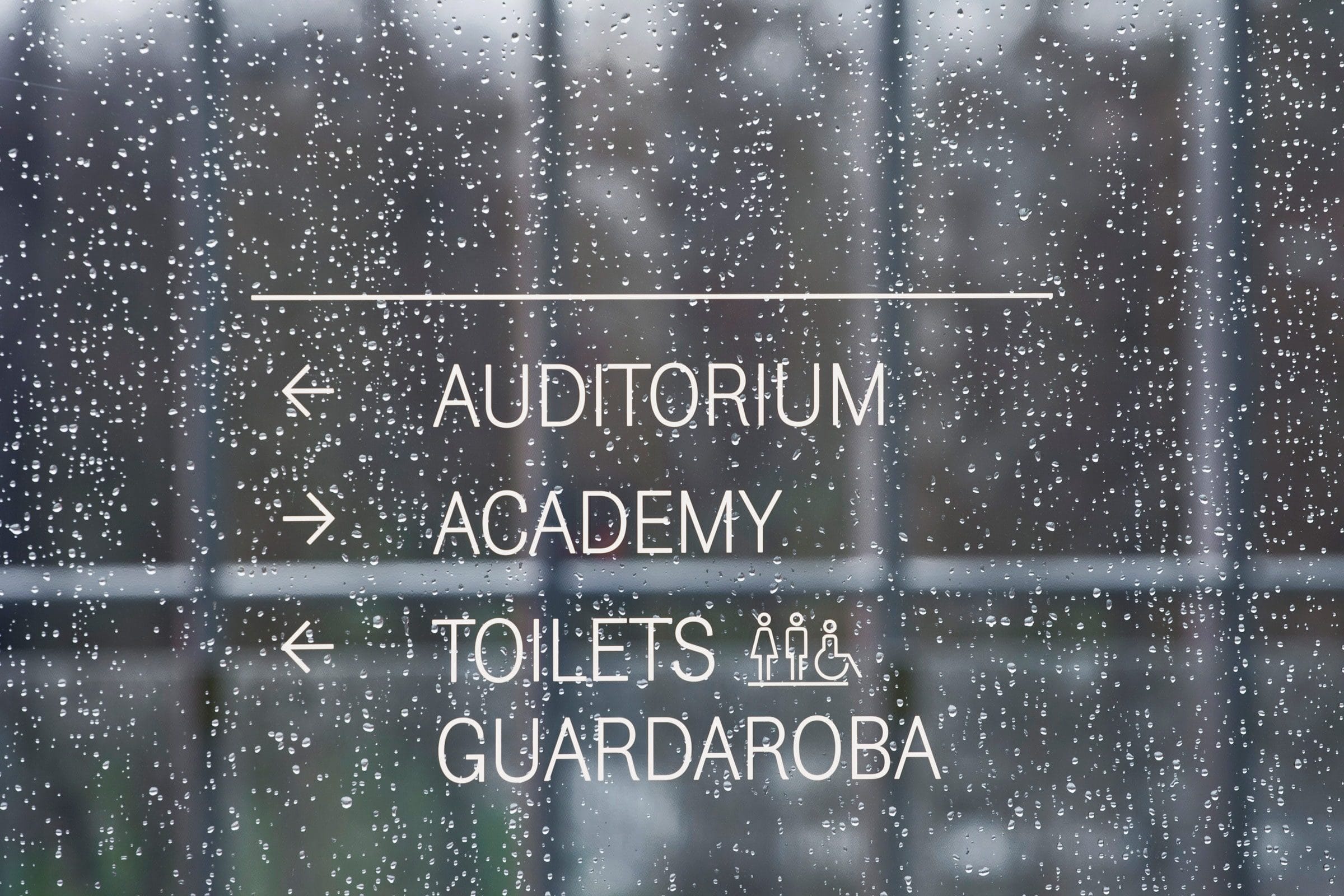 Frecce e scritte bianche su una vetrata: Auditorium, Academy, Toilets, Guardaroba