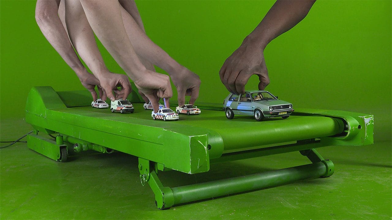 Mani che posano automobiline su un nastro verde davanti a un fondo verde