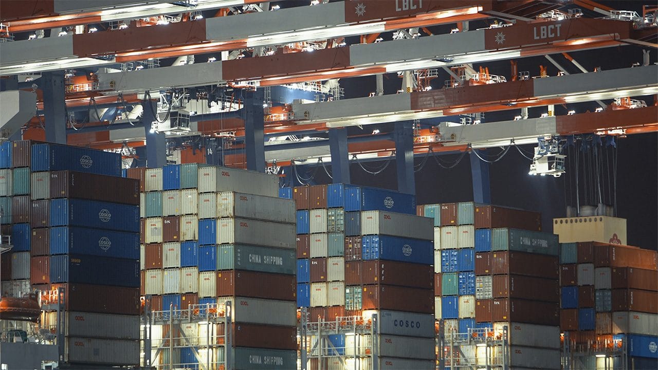 Container colorati impilati sotto le gru di un porto, di notte
